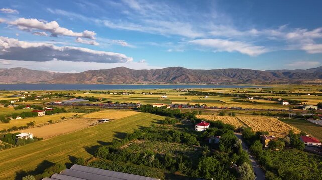 Majestic cinematic drone movement slowly panning right, revealing vast agricultural fields, a busy railway with a passing train, a parallel road, and a winding river leading to the horizon. 