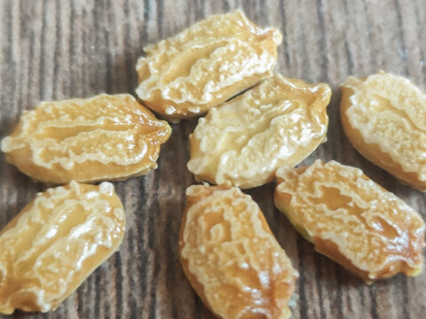A close-up macro shot of textured bitter melon (Momordica charantia) seeds scattered on a brown wooden surface. The unique, intricately patterned seeds, also known as karela, are shown in sharp detail