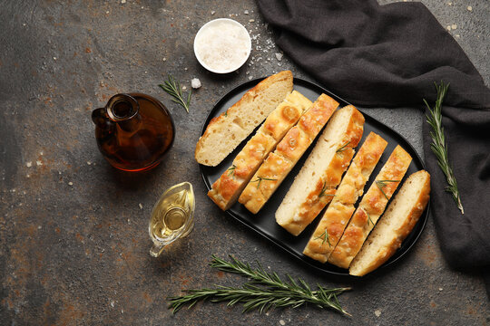 Plate with pieces of traditional Genovese focaccia and ingredients on black grunge background