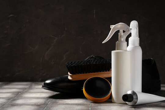 Shoe polishes with brush and shoes on grey tile table against black background