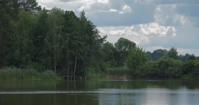 Static tripod shot of a peaceful lake with a small wooden pier on the bank