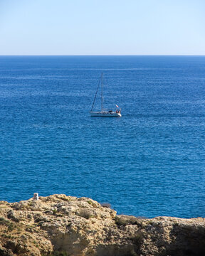 Elegant monohull sailing yacht with a single tall mast and a blue mainsail cover cruising on the calm waters of the Mediterranean Sea.