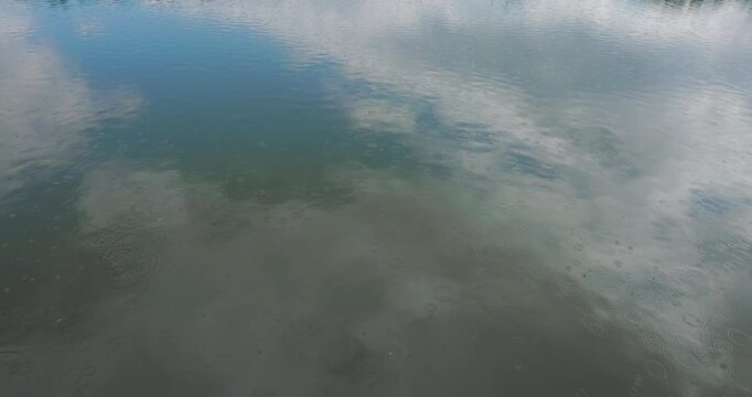 Raindrops falling on a lake water surface with sky reflection