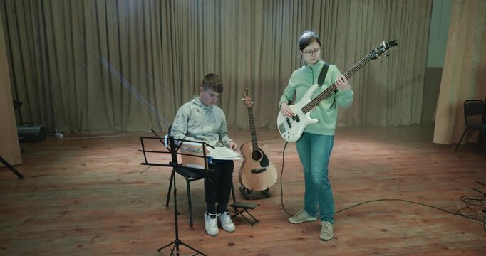 Boy and Girl Practice Playing Music on Stage. Kids Play Guitar and Bass Guitar. 4K 10-bit