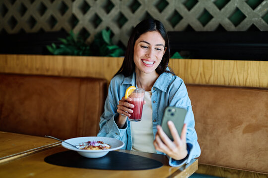 Young woman enjoying eating lunch and using a mobile phone at restaurant