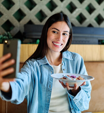 Young woman enjoying eating lunch and using a mobile phone and taking a selfie  at restaurant