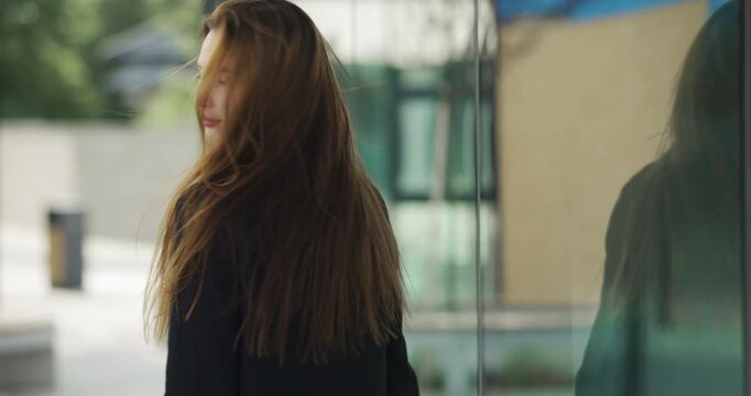 Close up portrait of attractive girl in black jacket looking back on urban street, slow motion