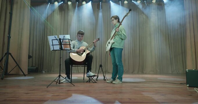 Boy and Girl Practice Playing Music on Stage. Kids Play Guitar and Bass Guitar. 4K 10-bit