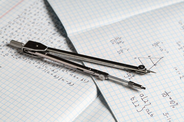 Obraz premium Copybooks with handwritten maths formulas and pair of compasses as background, closeup