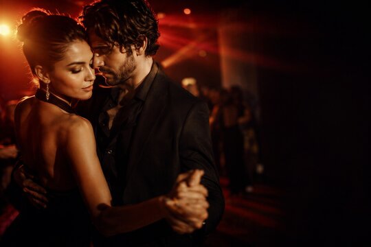 Young woman and man dancing tango in nightclub. Romantic couple in elegant clothes enjoying intimate moment on party floor.