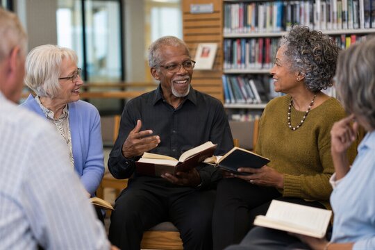 Senior group sitting in a circle to discuss books in a library. African American man and several caucasian woman talking together.