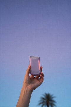 Woman hand holding modern flip phone against clear blue sky. Compact mobile device with sleek design. Technology communication and travel lifestyle concept for digital connectivity