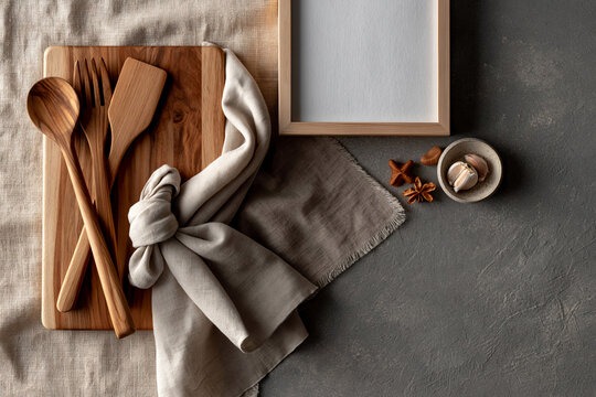 Wooden kitchen tools and a blank frame on a table with cloth and spices in a well-arranged kitchen setting