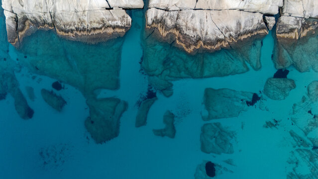 Aerial view of turquoise water and submerged rocks along the coast of Mandrakia, Milos, Greece.