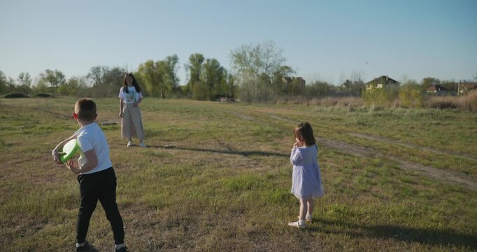 Mother with Children Throw Flying Disk Playing Outside. Family spend time together on nature. 4K 10-bit