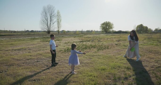 Mother with Children Throw Flying Disk Playing Outside. Family spend time together on nature. 4K 10-bit