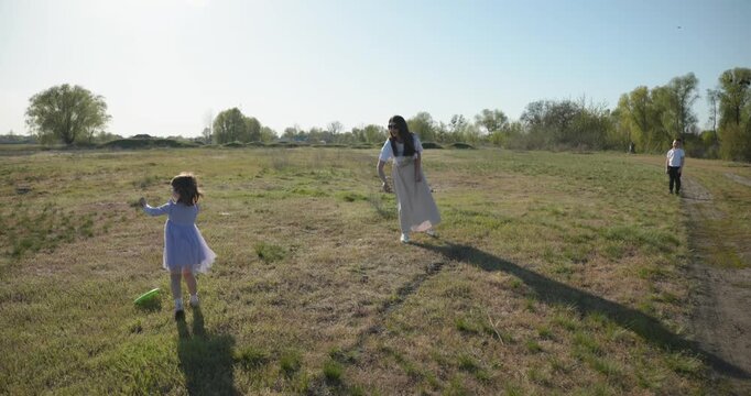 Mother with Children Throw Flying Disk Playing Outside. Family spend time together on nature. 4K 10-bit