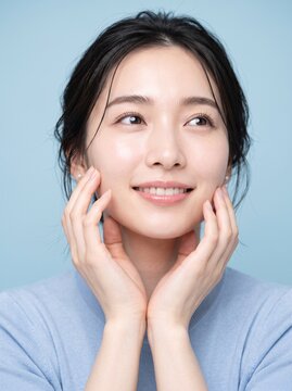 Young Japanese woman touching jawline in natural daylight at home, skincare routine and self care concept, well suited for lifestyle and beauty blogs