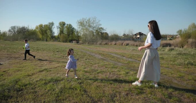 Mother with Children Throw Flying Disk Playing Outside. Family spend time together on nature. 4K 10-bit