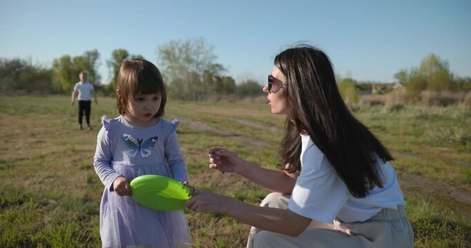 Mother with Children Throw Flying Disk Playing Outside. Family spend time together on nature. 4K 10-bit