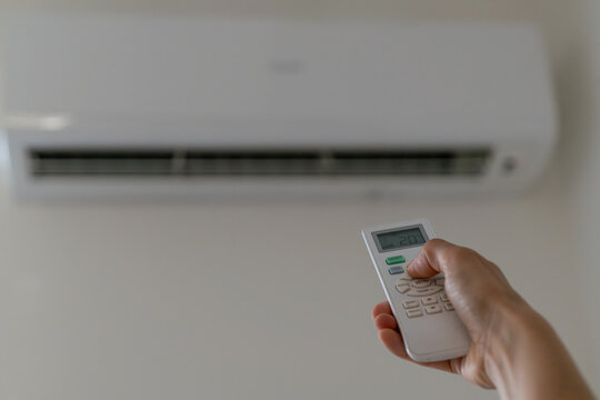 Hand adjusting an air conditioner remote control set to 20 degrees Celsius. Home climate control, cooling system, energy efficiency and indoor comfort with copy space.