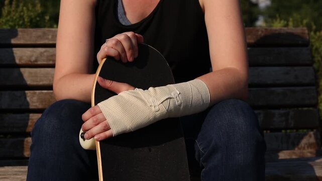 Wrist injury sustained while skateboarding. Close-up of girl's hand wrapped in elastic bandage, wooden skateboard next to it. Concept of sports injuries, first aid and safety during extreme sports