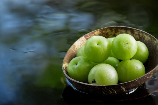 Phyllanthus emblica or Indian Gooseberry fruits placed on floating vessel against natural backdrop.