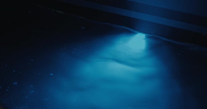 Blue underwater light beneath a yacht illuminates the surrounding seawater at night in a marina.
