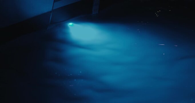 Blue underwater light mounted on a yacht illuminates the surrounding seawater at night in a marina.