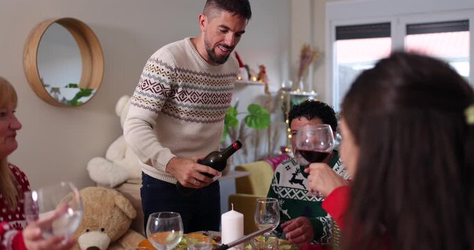 Happy family gathering for christmas dinner while a man pours red wine into glasses