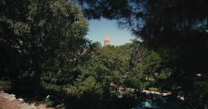 A church bell tower rises above the treetops of Queen Jelena Madijevka Park in Zadar Croatia.