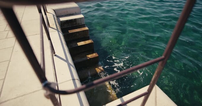 Stone sea access stairs with a metal handrail lead into the clear Adriatic Sea along the waterfront in Zadar Croatia.