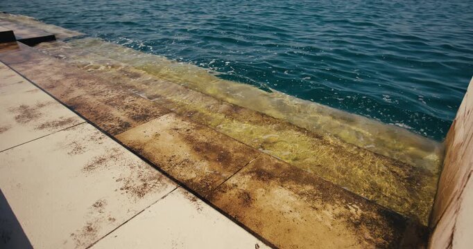 Sea waves wash over the lower stone steps of the Sea Organ waterfront installation in Zadar Croatia.