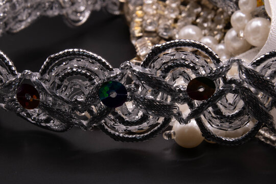 Wavy silver braided trim with colorful sequins resting in front of white pearls and craft accessories