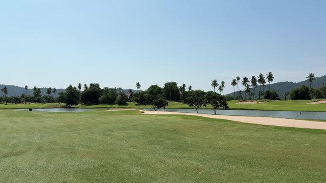 Slow panning view of tropical golf course with lake, bunkers and mountain scenery in Thailand