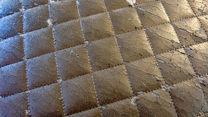Obraz premium Worn quilted brown synthetic leather upholstery with cracked texture and peeling surface showing damage from wear, a deteriorating fabric background