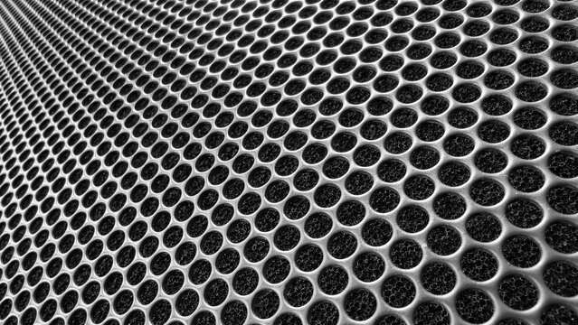 Close up of a perforated metal grid or speaker grill, creating a textured pattern with numerous symmetrical circular holes providing a modern industrial background
