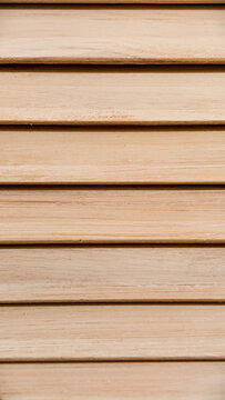 Close up view of natural wood louver patterns, forming a textured background with horizontally arranged light brown wooden slats and visible grain