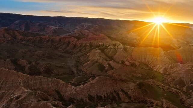 Aerial view of rugged mountain terrain bathed in warm golden sunlight during a dramatic sunset in Xinjiang.