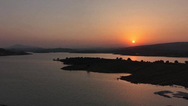 High altitude aerial drone shot over a vast lake with silhouetted islands at sunset.