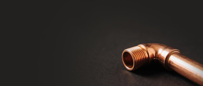 Angled copper pipe fitting with threads on a dark gray background, highlighting industrial and plumbing components.
