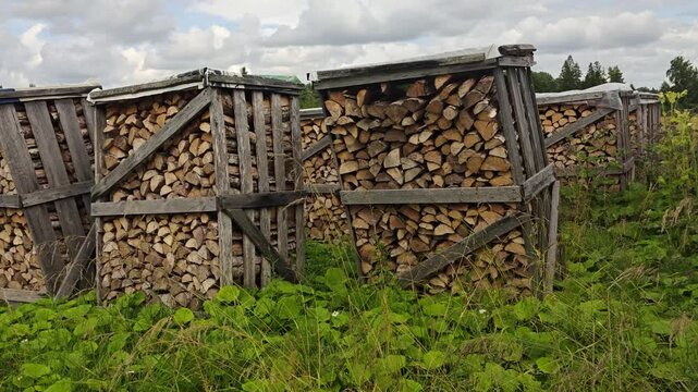 Stacked firewood stored in wooden racks outdoors. Split logs prepared for heating in a rural environment under a cloudy sky.