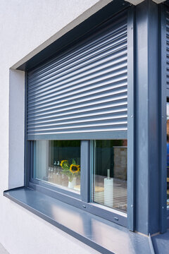Partially lowered exterior roller shutter shades kitchen window with sunflowers and paper towel roll visible inside