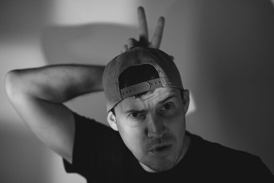 Young man in baseball cap making bunny ears gesture over head. Portrait of playful guy acting silly and looking into camera. Concept of humor, fun lifestyle and casual expression.