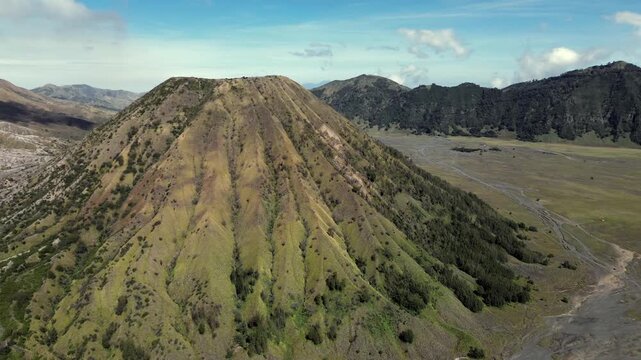 Scenic aerial view of Mount Batok inactive volcano cone with green slopes in East Java, Indonesia