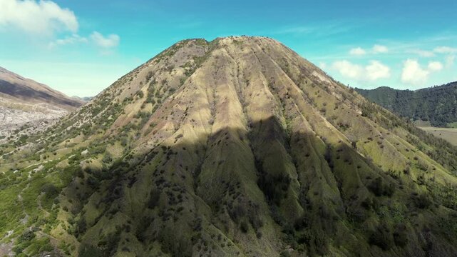 Cinematic 4K aerial shot flying forward towards the scenic Mount Batok inactive volcano, revealing its textured green slopes in East Java, Indonesia.