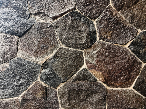 High-detail full-frame view of a decorative stone wall made from irregular natural slate and basalt tiles, showcasing warm earthy tones and rugged mineral surfaces.