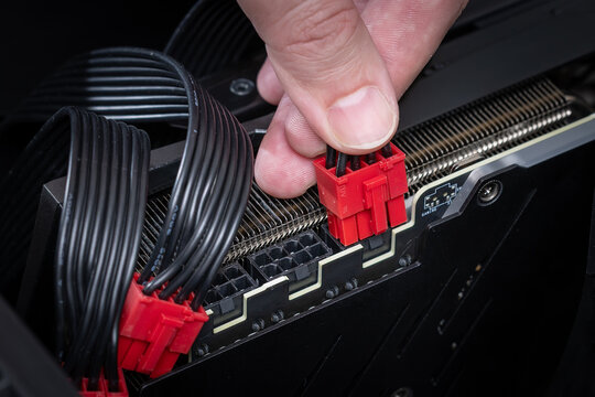 Close up of a hand connecting red modular PCI power connectors to a powerful graphics card inside a PC case. Building or upgrading a powerful gaming PC