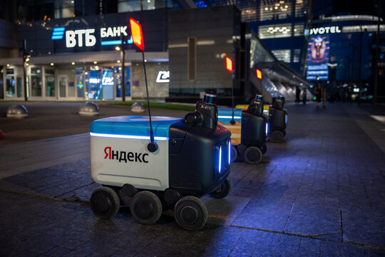 Yandex delivery robots wait for assignments on a city sidewalk in the evening. Autonomous delivery of goods and groceries. Moscow, Russia - June 22, 2024