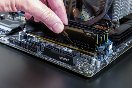 Technician installs a black DDR memory module into a motherboard DIMM slot. Assembly or upgrade of a modern PC. Expensive PC components